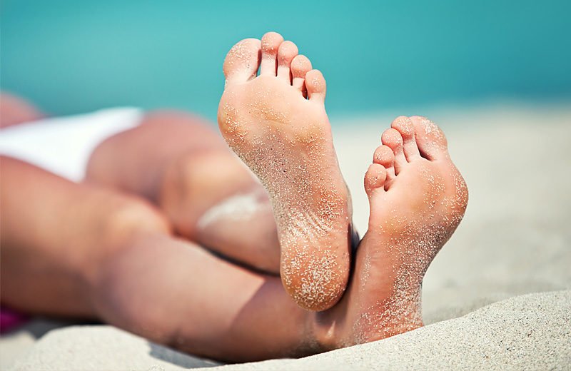 A colour image of the tanned legs and feet of a person lying on a beach after receiving spray tanning by Vicki Hooper Beauty - Grayshott & Headley Down